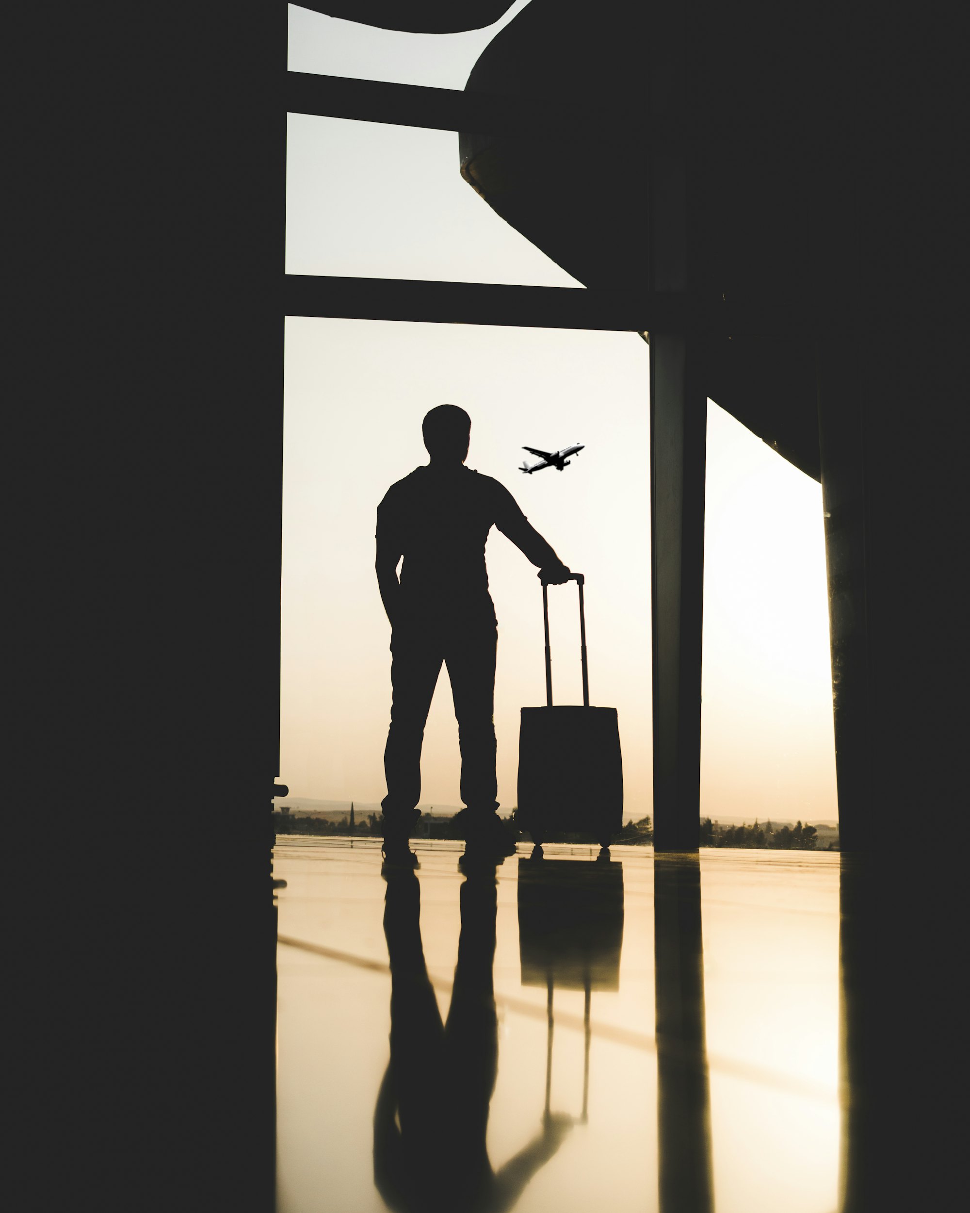Traveler silhouetted against an airport window as a plane takes off