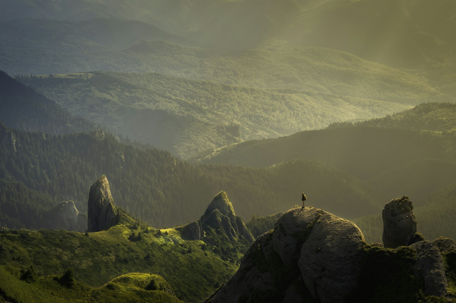 Lone hiker on a ridge above a misty green valley